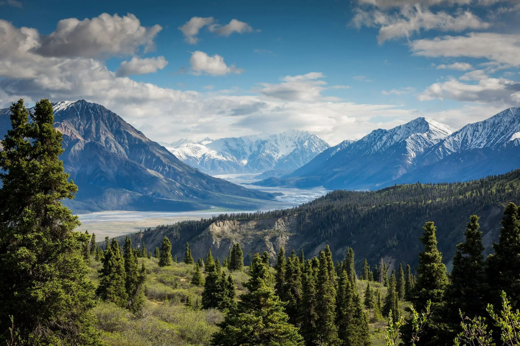 Mountain peaks above a forested valley beneath scattered clouds