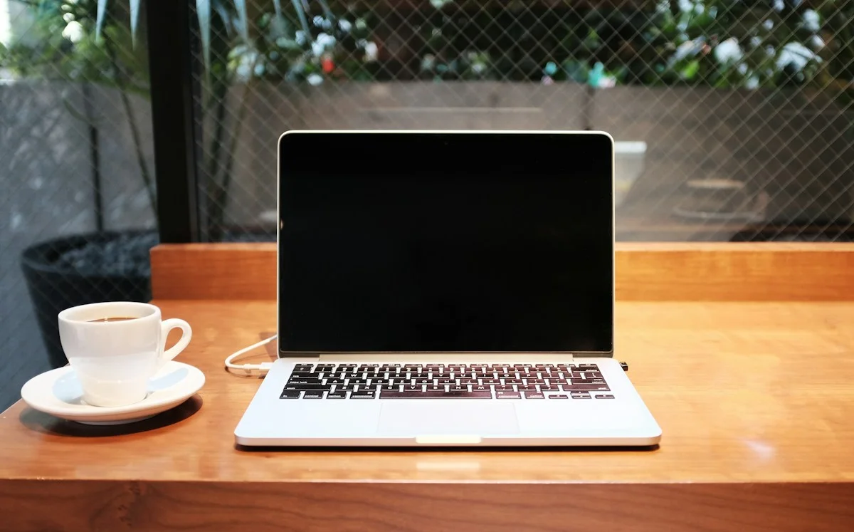 Laptop and coffee on a wooden table beside a window