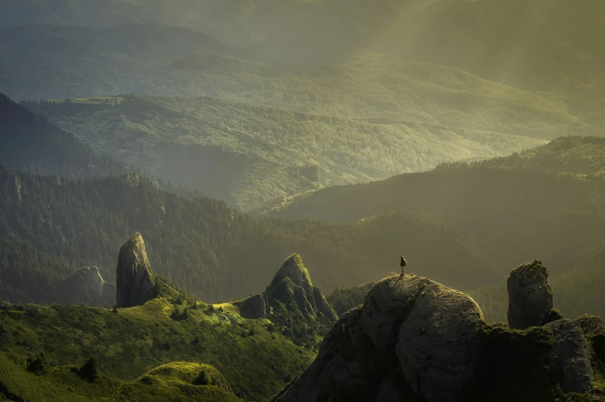 Small traveler silhouetted on a rocky ridge above a sunlit mountain valley